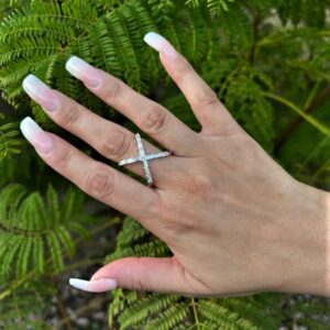 Hand with long, manicured nails and a starfish ring on a green leafy background.
